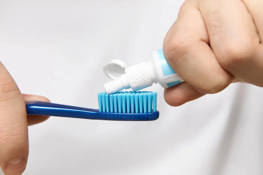 A person squeezing toothpaste onto a blue toothbrush.