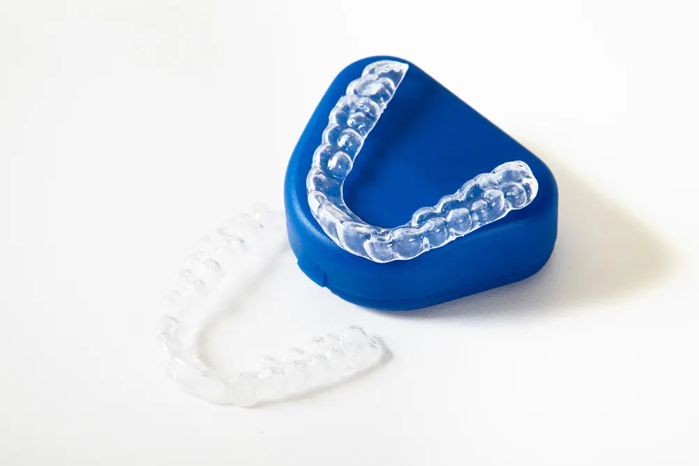 Invisalign clear dental aligners, one placed on a blue container and the other lying beside it on a white surface at Queen City Orthodontics in Liberty Township and Hamilton OH