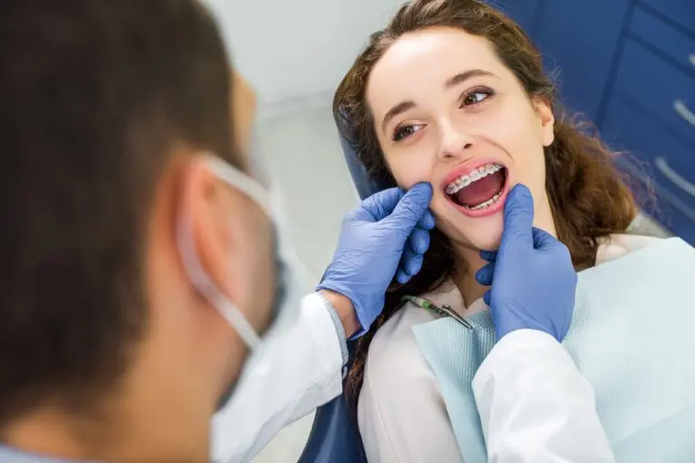 Dentist in gloves examining young woman with braces sitting in a dental chair.