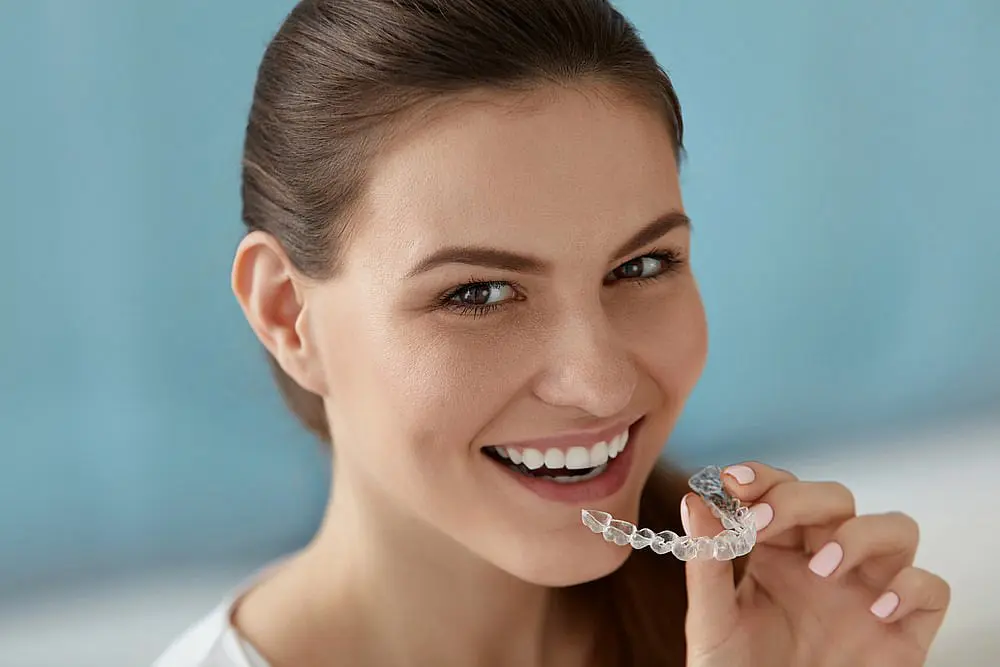 A person smiles while holding a clear Invisalign dental aligner in Hamilton, OH