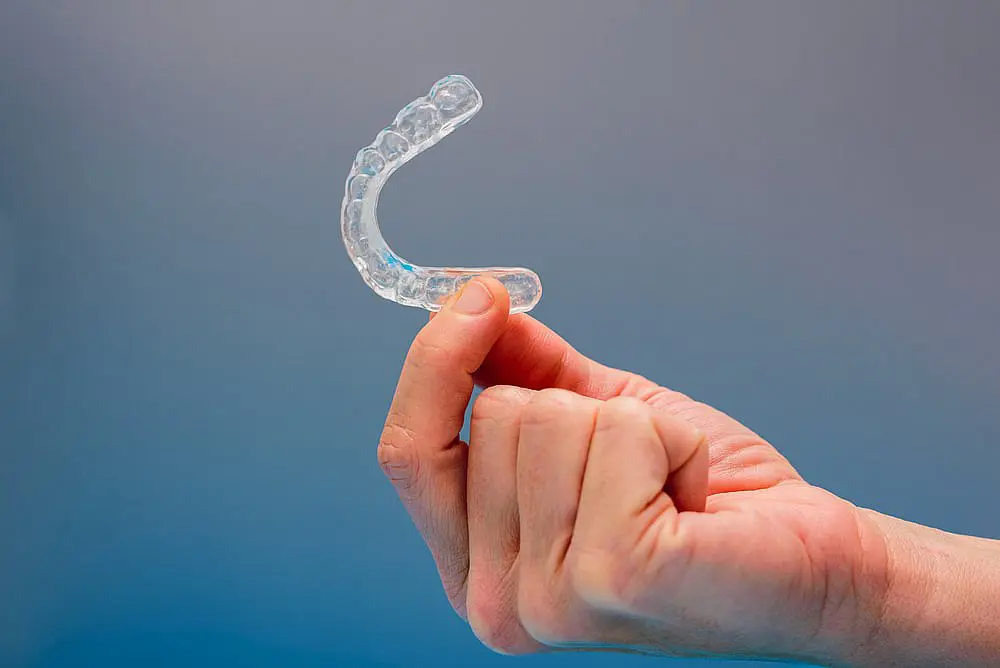 A hand holds an Invisalign aligner against a plain background in Hamilton, OH