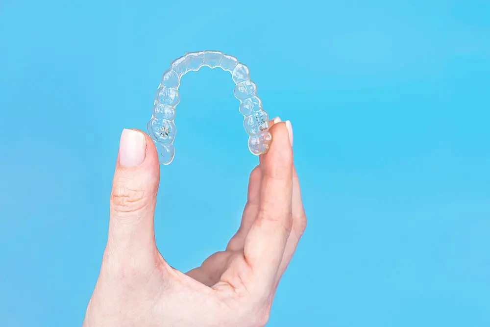 A hand gracefully holds an Invisalign dental aligner against a calming blue background in Hamilton, OH