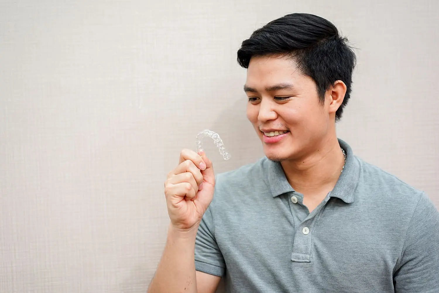 A man in a gray polo shirt smiles warmly, showcasing an Invisalign clear dental aligner against a neutral background in Hamilton, OH