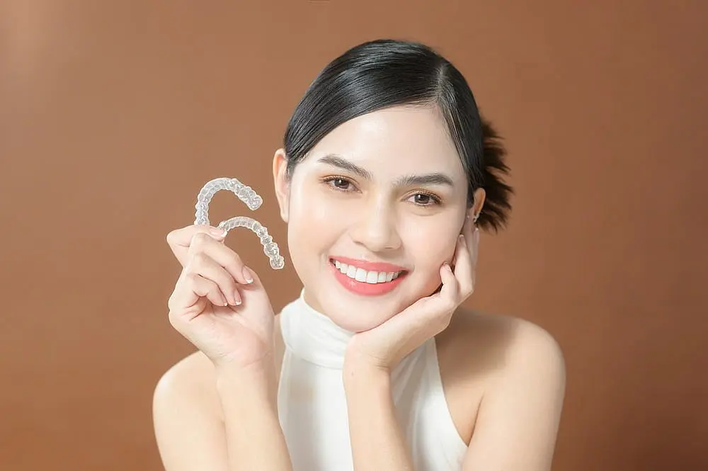 A person smiling and showcasing Invisalign clear dental aligners against a warm brown background as one of the Alternatives to Braces in Liberty Township or Hamilton, OH