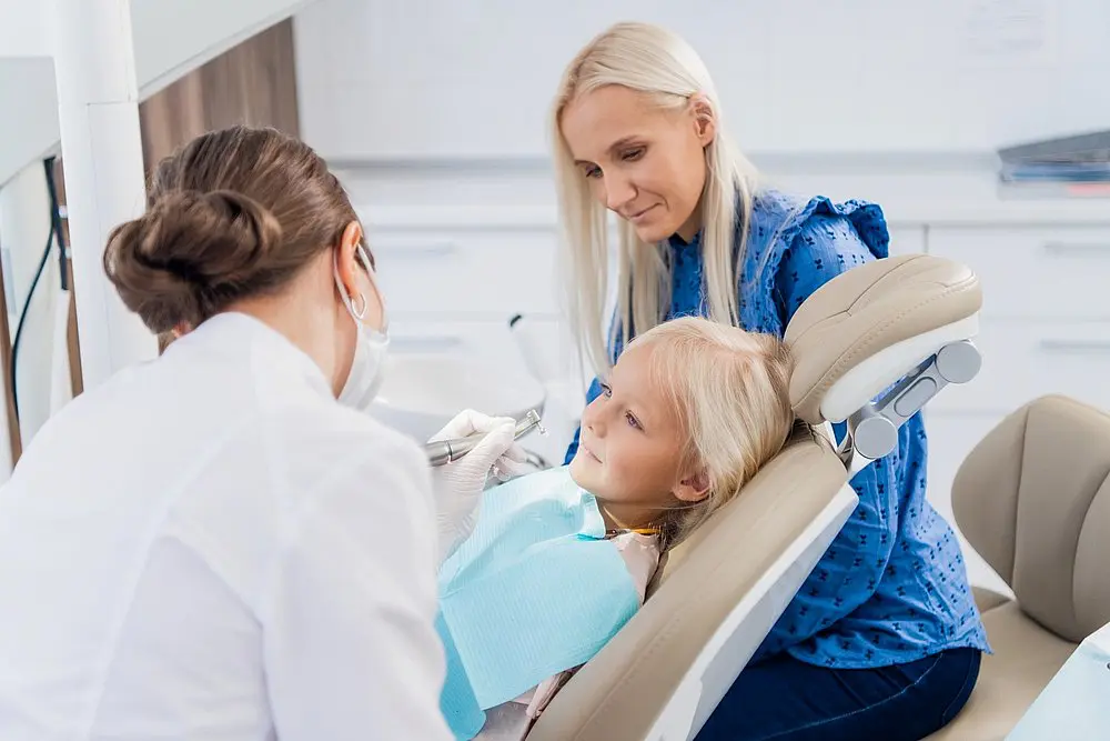 At Queen City Orthodontics one of the expert of how to fix overbite in Liberty Township or Hamilton, OH, a dentist examines a young girl’s teeth as her mother sits nearby.