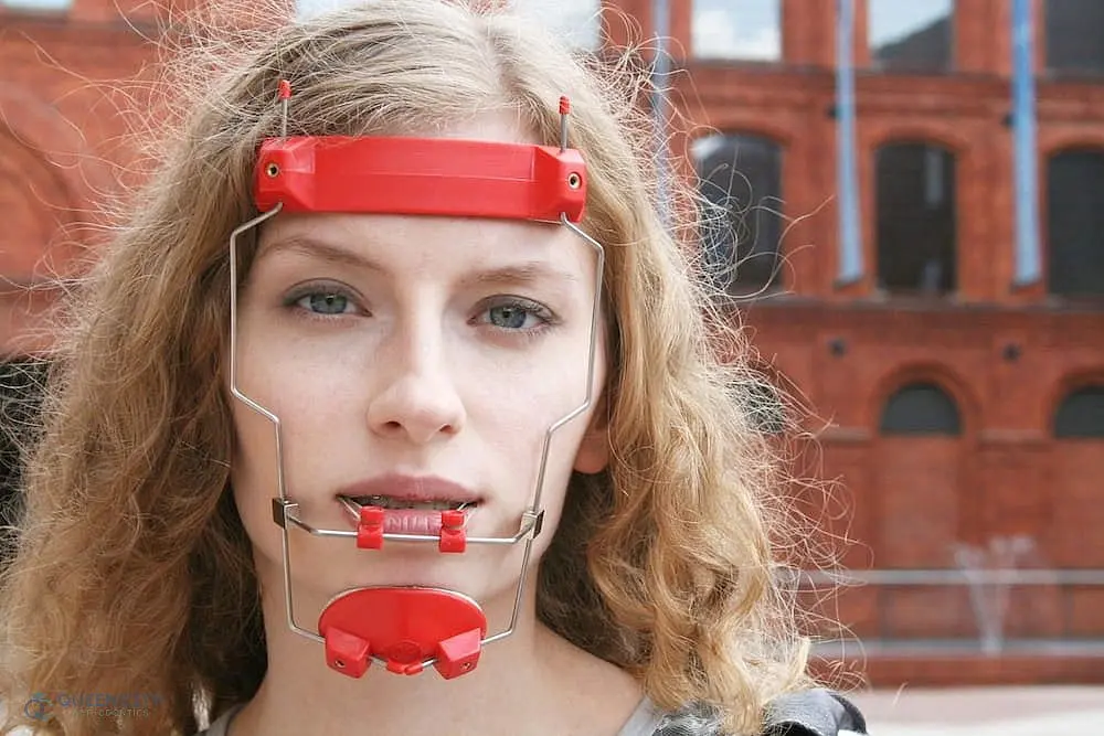 In front of a brick building, a person with wavy blonde hair is seen wearing a red Reverse Pull Headgear Braces in Liberty Township and Hamilton, OH—an example of treatments available