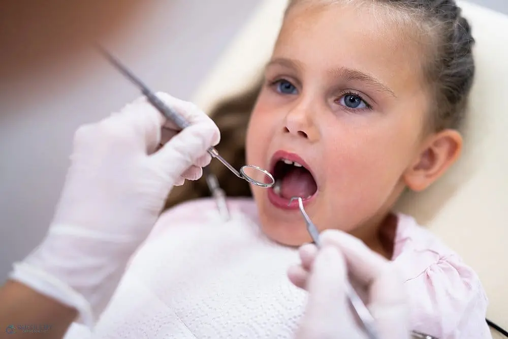 A dentist at Queen City Orthodontics examines a child's teeth using dental tools as a procedure of how to fix overbite in Liberty Township or Hamilton, OH.