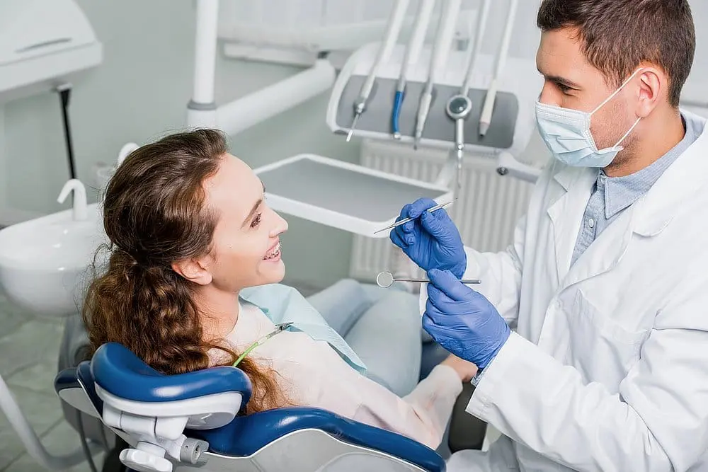A dentist at Queen City Orthodontics in Liberty Township or Hamilton, OH examines a smiling patient in a clinic, checking bite alignment - Overbite vs Underbite in Liberty Township and Hamilton, OH