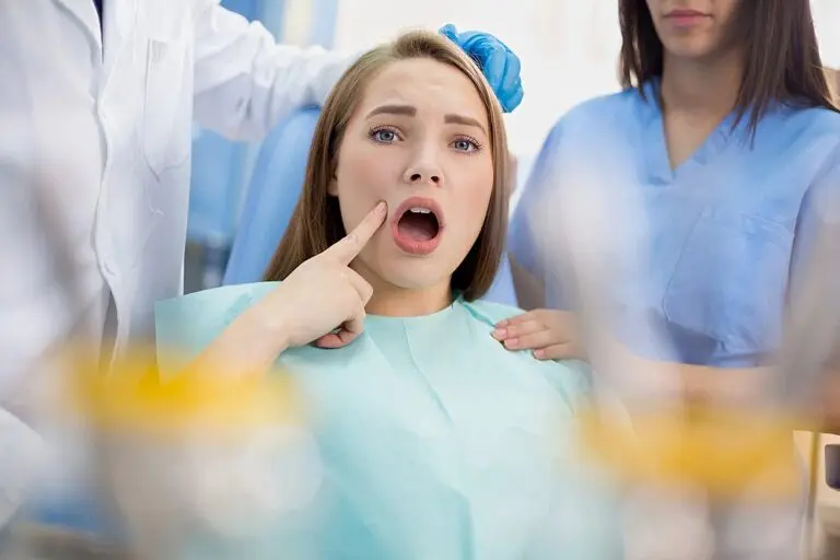 At Queen City Orthodontics in Liberty Township or Hamilton, OH, a woman points worriedly to her mouth as two dentists stand by - TMJ Treatment in Liberty Township and Hamilton, OH