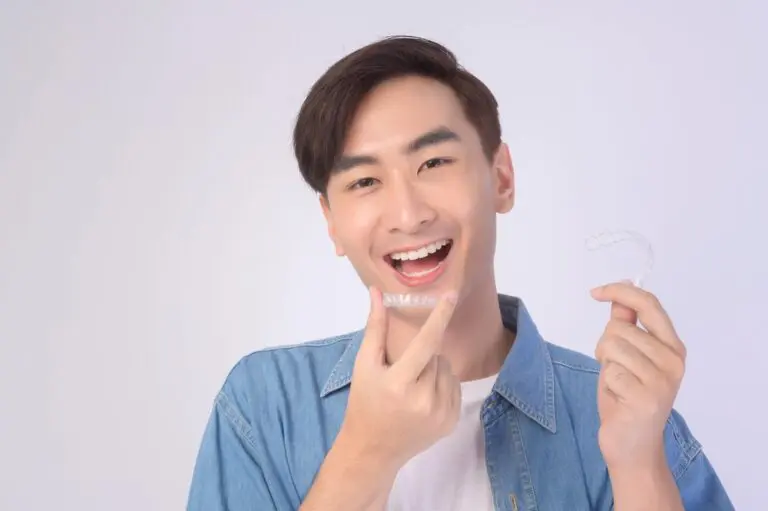 At Queen City Orthodontics in Liberty Township or Hamilton, OH, a person smiles while holding and fitting clear aligners, in casual attire - How Long Does Invisalign Take in Liberty Township and Hamilton, OH