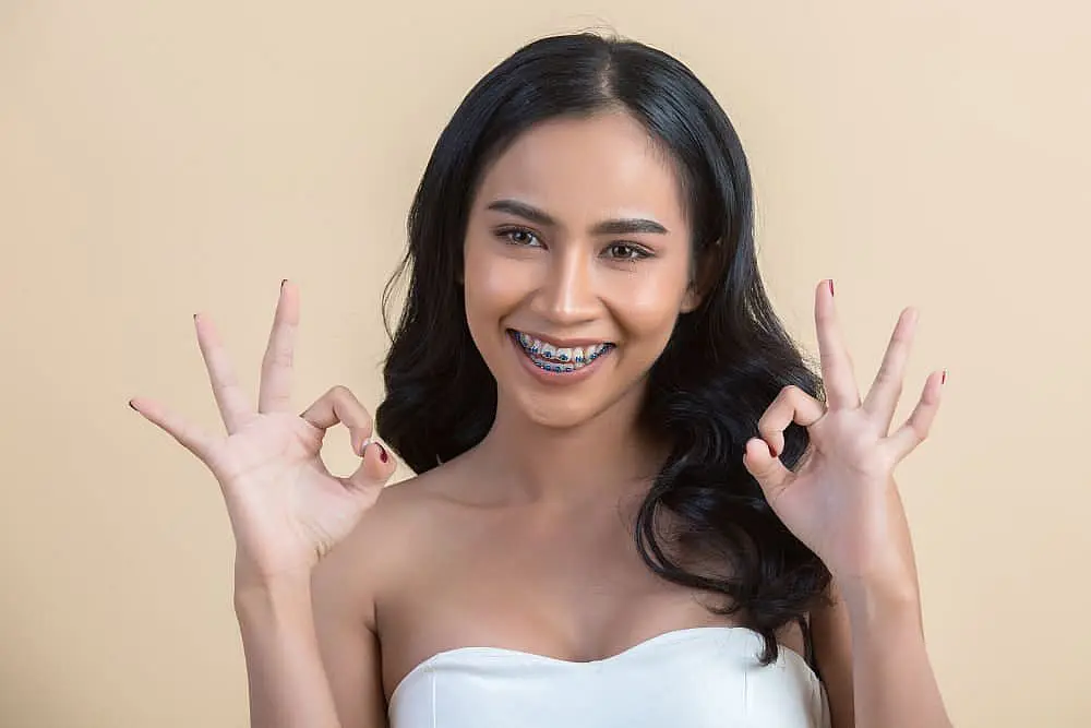 A smiling woman with braces shows "OK" signs, promoting Queen City Orthodontics in Liberty Township or Hamilton, OH.