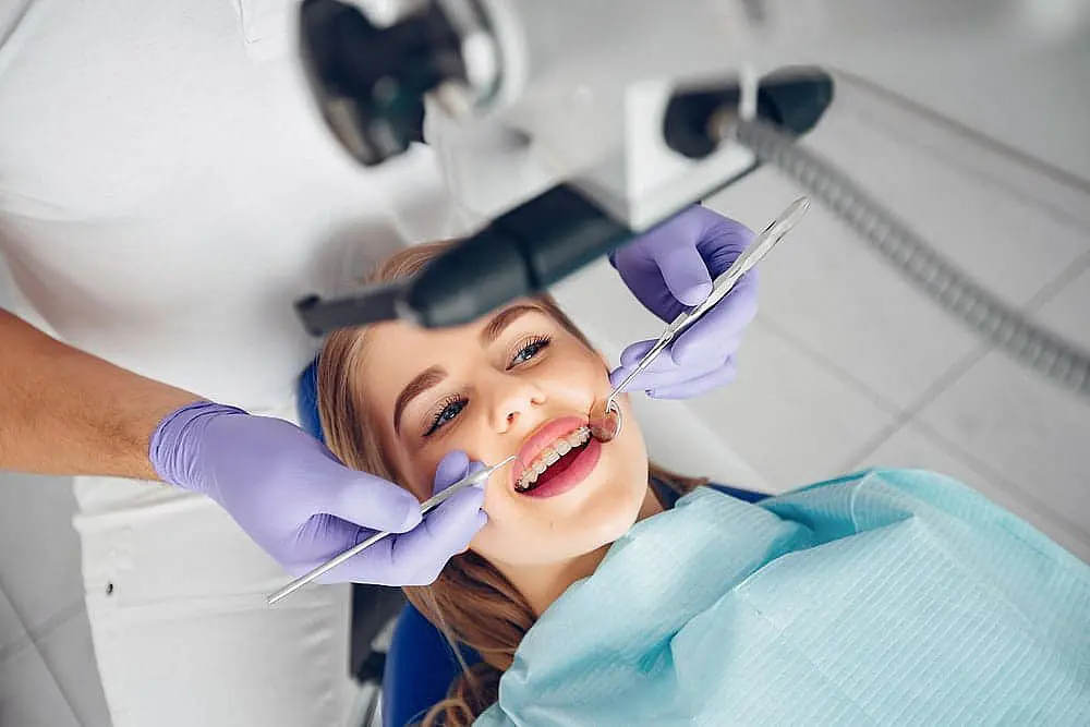 Person receiving a dental check-up, with dentist examining teeth using dental instruments while wearing purple gloves in Liberty Township and Hamilton, OH.
